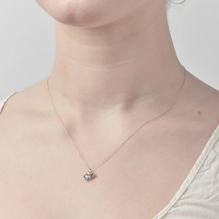 Asymmetric sapphire pendant with golden granules and single white diamond, on a fine link chain with toggle clasp, on model 