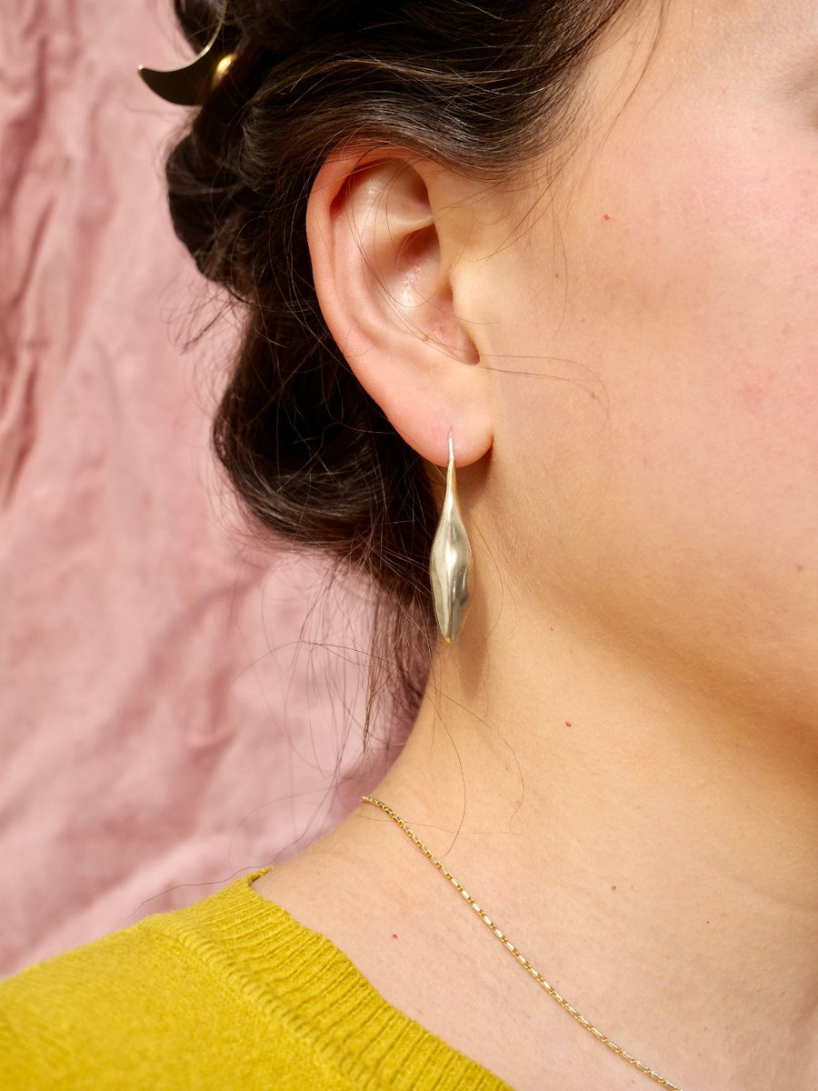olive leaf earring on ear with pink backdrop