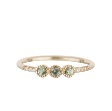 3 light green sapphires set in milgrain detailed bezel settings in a row at the center of a thin gold band. To add even more texture, there are three additional smaller white diamonds flush set into the band on either side of the large central diamonds. The slight texture makes this otherwise clean design feel ever so intimate.