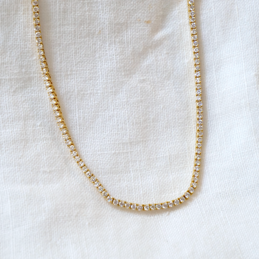 4 Prong Tennis Necklace with 5ct of white Diamonds, 16 inches long, on white linen backdrop 