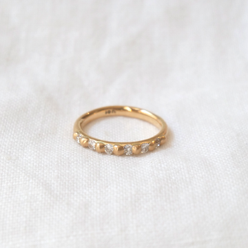 A close-up of a delicate gold ring with small antique Mine Cut diamonds, set against a soft white fabric background by Marisa Mason Jewelry's Cora Classic - Antique Diamonds.
