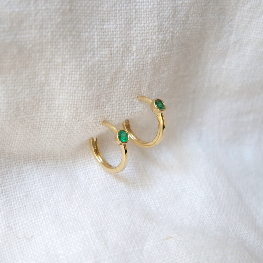 Sweet every day little clicker hoops with a single 2.7mm bezel set emerald in each. Shown on white backdrop.
