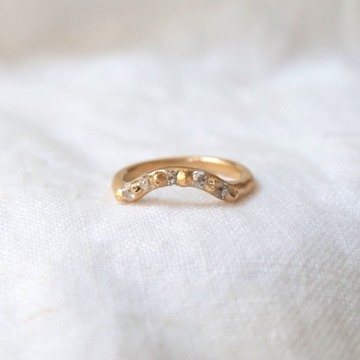 Rounded gold band with carved gold granulation details used to set five diamonds stones, creating a curve in the band that makes room for wearing with a solitaire ring