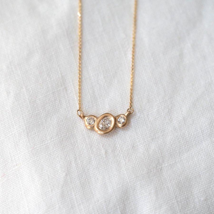 Organically sculpted 3 stone necklace, with one larger oval cut diamond and 2 small round diamonds on either side, bezel set in 14k yellow gold.  