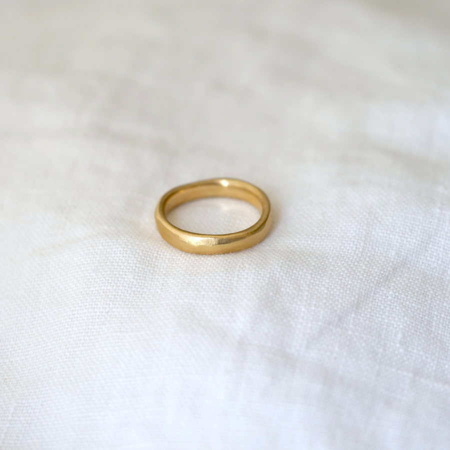 A classic gold band but with a much more organic look through uneven edges, dimpled texture surface, and a general 