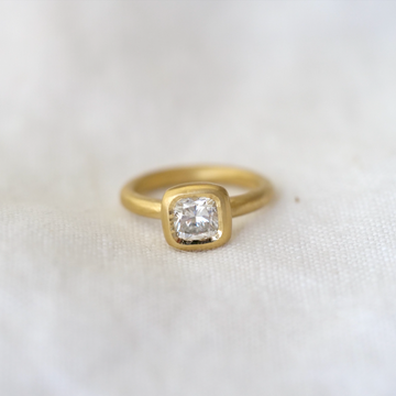 cushion cut diamond is bezel set in luxurious 18k gold