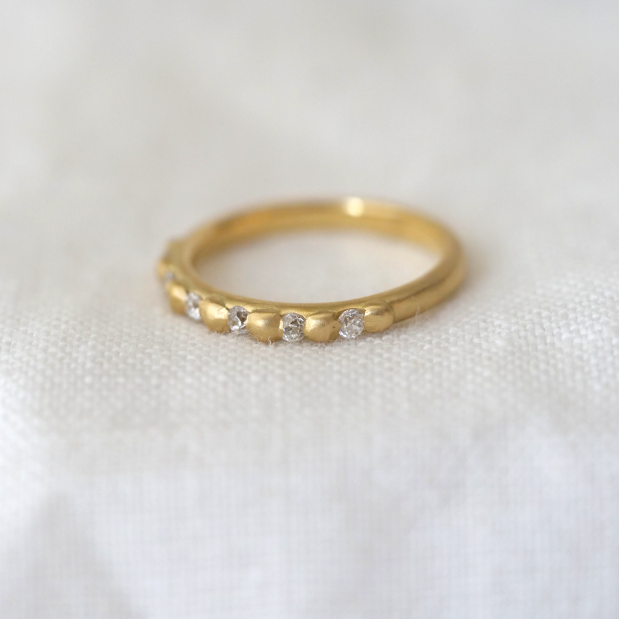 Rounded gold band with carved gold granulation details used to set six white diamonds stones
