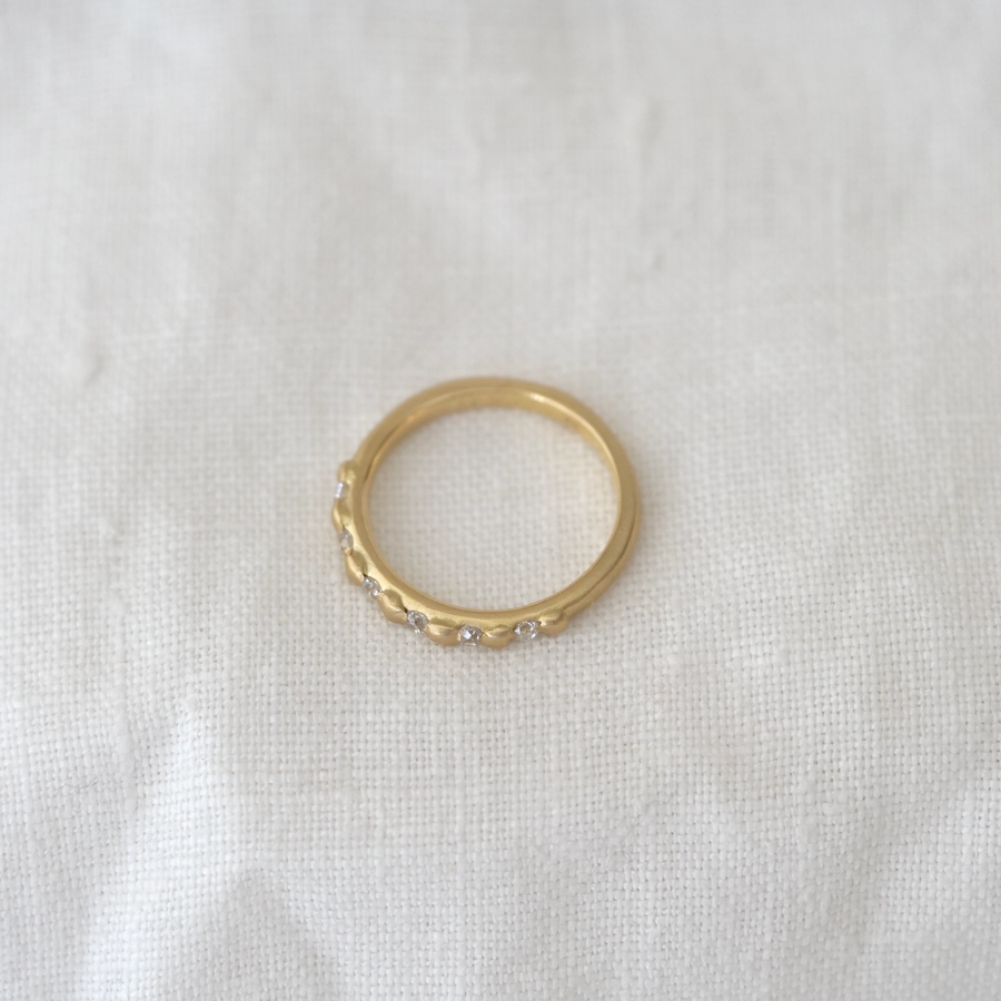A Marisa Mason Jewelry Cora Classic 18k gold ring with white diamonds on a white fabric surface.