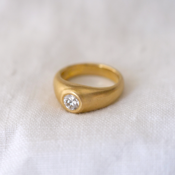 A natural, slightly domed shaped features a dazzling white diamond flush set into the rich 18k band