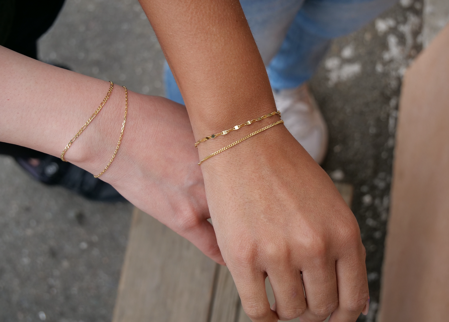 Two wrists with delicate gold bracelets on