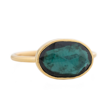 gold ring with one bezel set dark blue green tourmaline. The stone comes in a gradient of dark blue teal. 