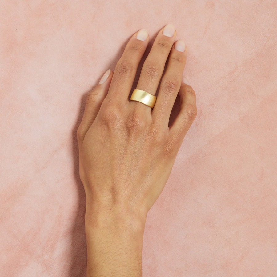 extra wide, solid gold band with slight irregular texture around the edge and surface on models middle finger 