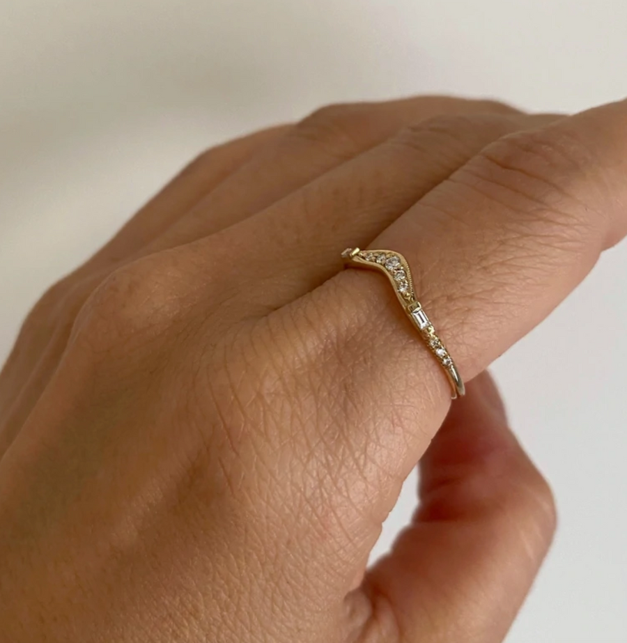 A thin band curved at the center with 5 round white diamonds, two baguette diamonds on either side, and then 6 little round diamonds bead set in the band on model 