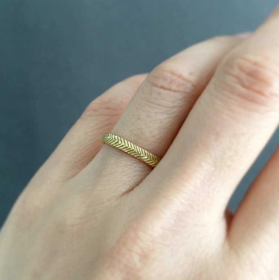 2.5mm wide 18k gold band with herring bone pattern etching all around on the face on model