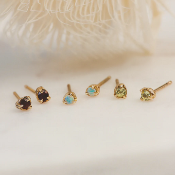 14k Gold Birthstone Studs shown on white backdrop. Three pairs: red garnet, blue opal and green peridot 
