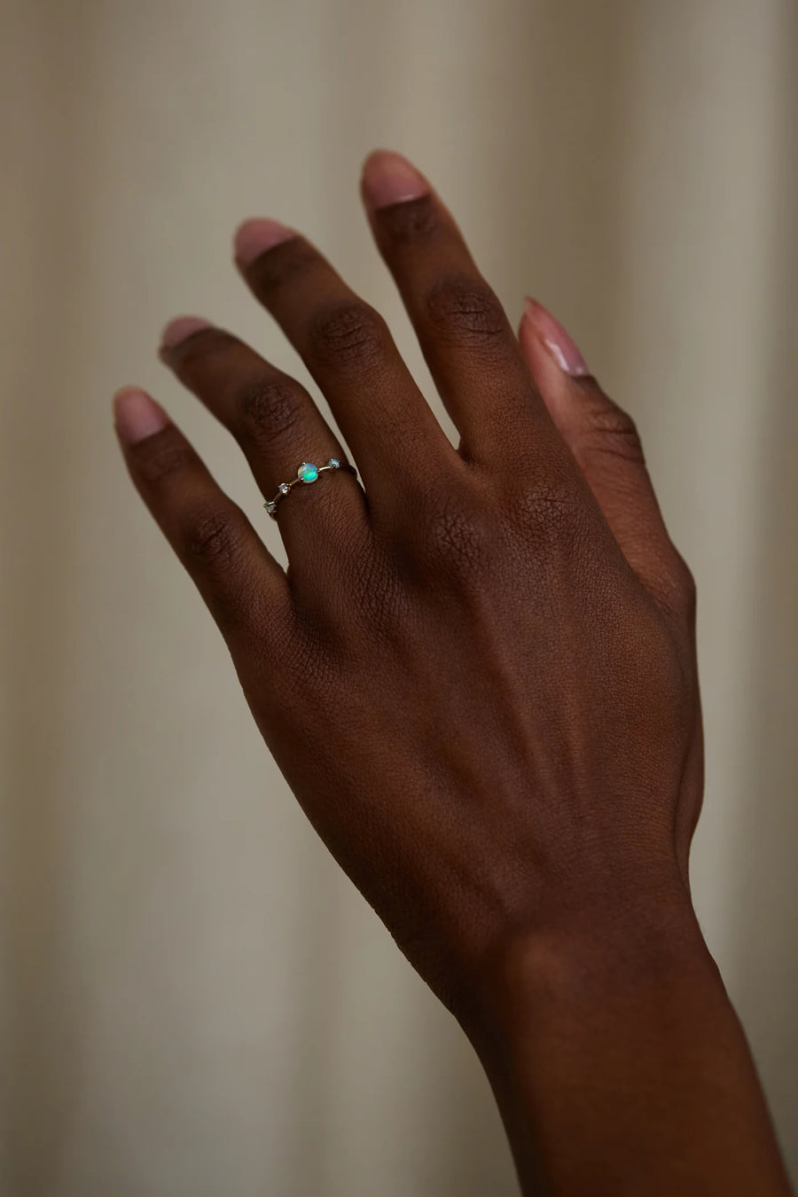 Hand wearing a ring with a green gemstone against a neutral background