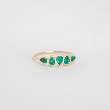 Gold ring with teardrop shaped green gemstones on a gray background