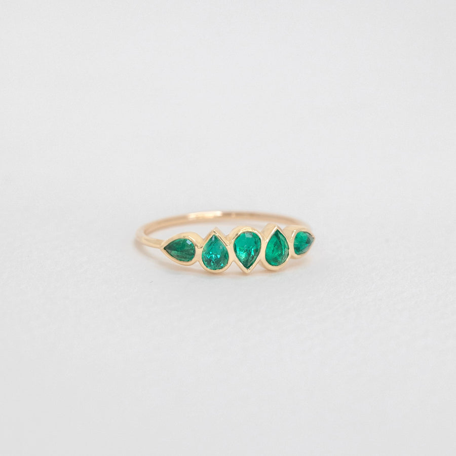Gold ring with teardrop shaped green gemstones on a gray background