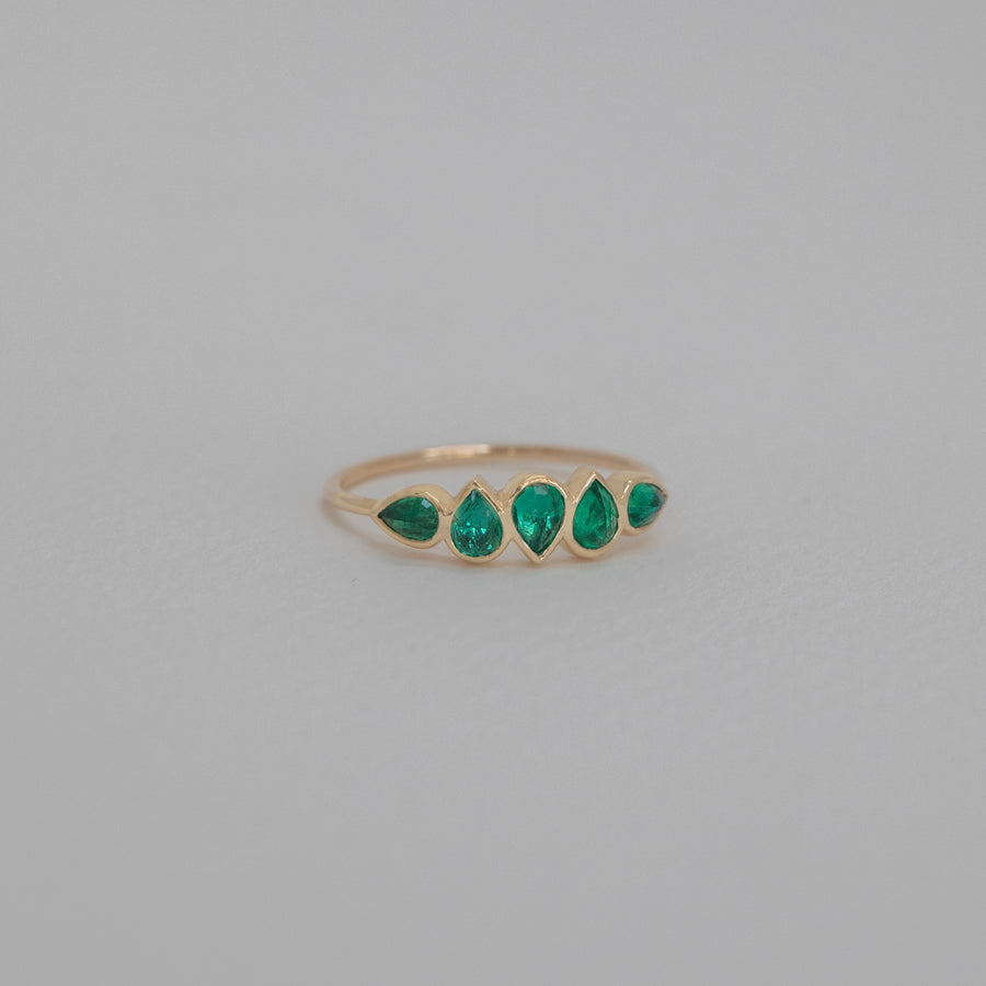 Gold ring with teardrop shaped green gemstones on a gray background
