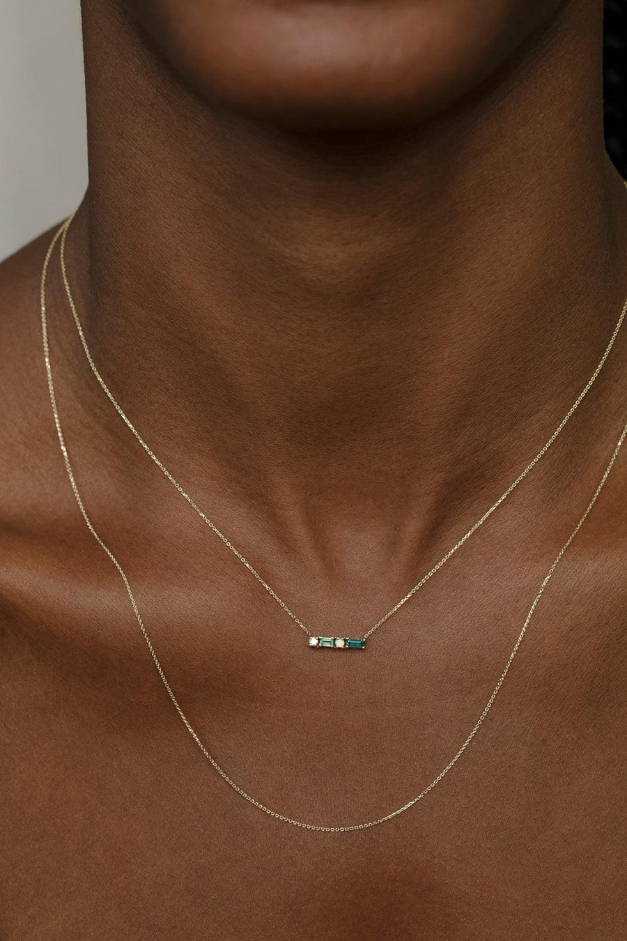 Gold necklace with a small pendant on a person's neck against a neutral background