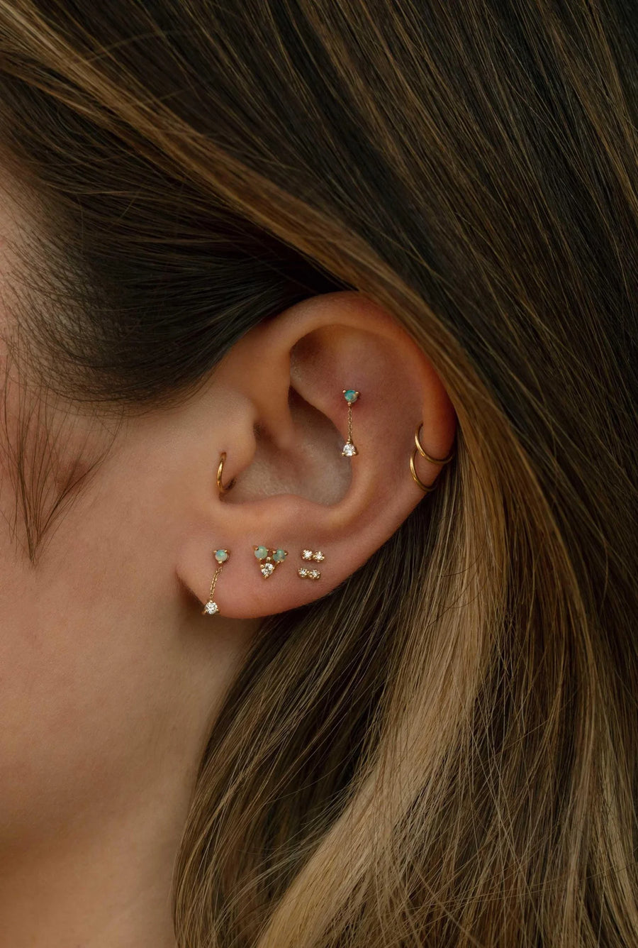 Close-up of an ear with multiple earrings and hair details.