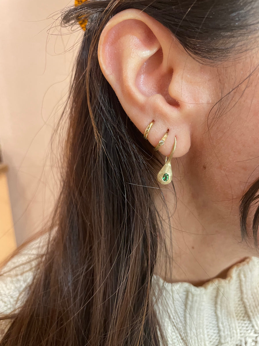 Close-up of an ear wearing gold hoop earrings with a green gemstone.