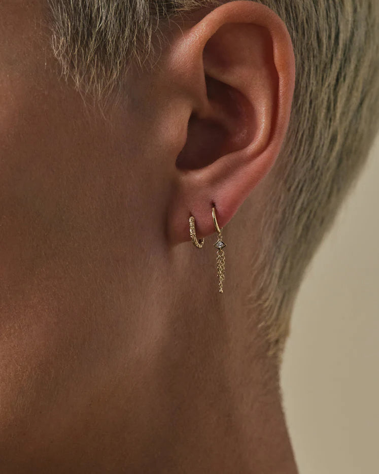 Close-up of an ear wearing a gold hoop earring with a blurred background