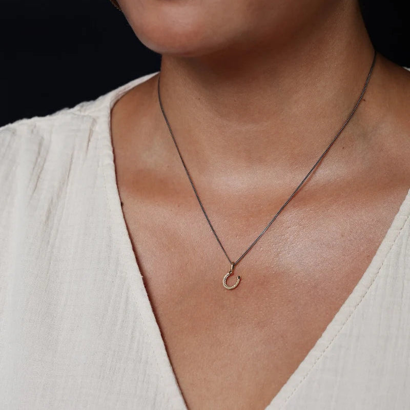 Necklace with a small pendant worn by a person in a white top against a black background