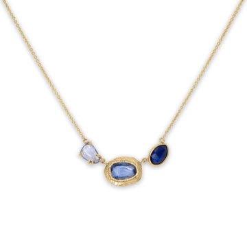 A triple sapphire necklace with freeform cut blue sapphire stones set in 18 karat yellow gold, displayed on an adjustable 16-18 inch chain.