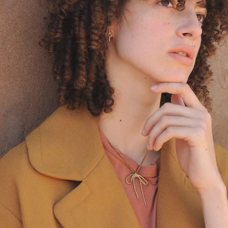 Woman wearing a gold necklace with a bow design, against a neutral background