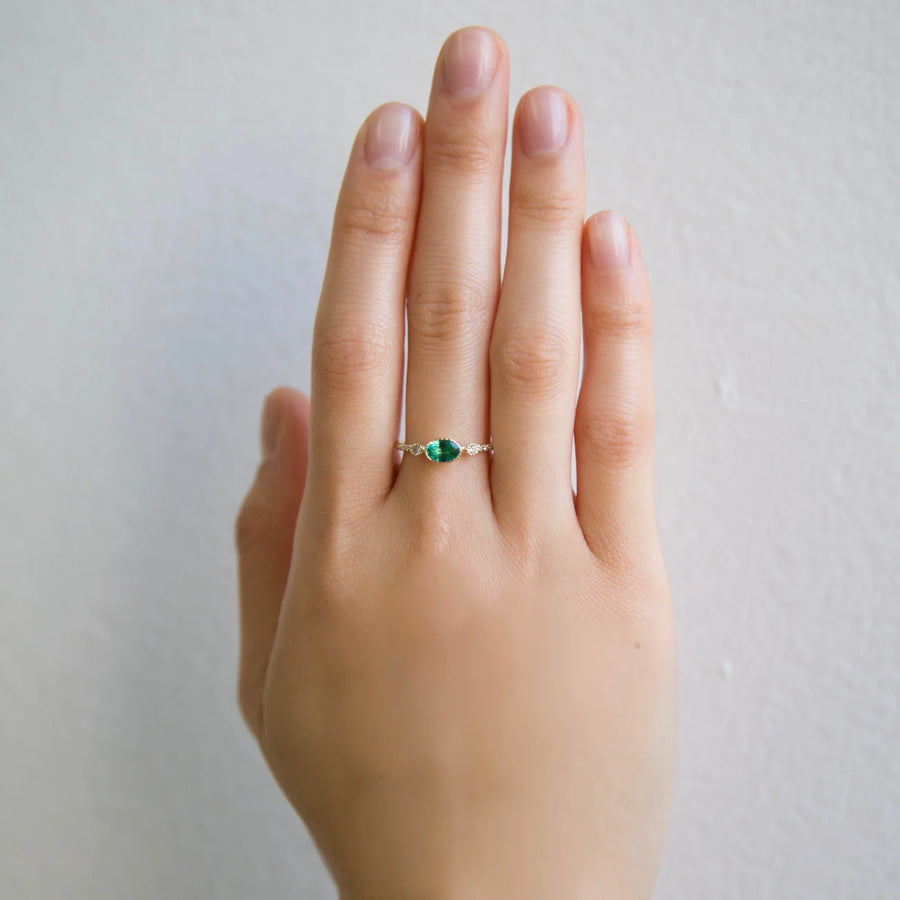 A vibrant emerald set in a bezel setting with engraved lines, flanked by two round diamonds and pave diamonds on either side, on hand