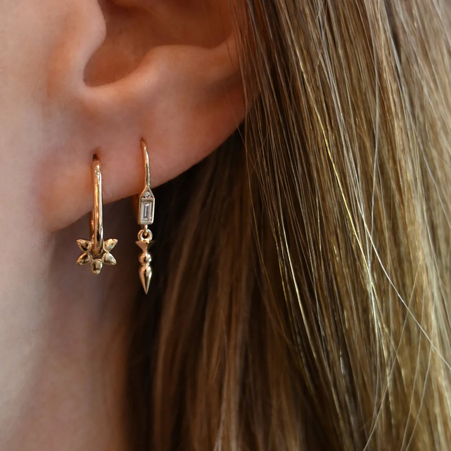 Close-up of a person wearing gold hoop earrings with intricate designs.
