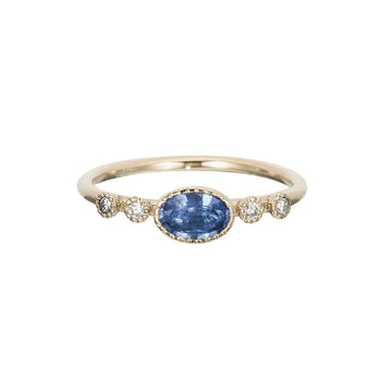 A thin gold band with a bezel set oval blue sapphire in the center, and two round white diamonds on either side.
