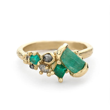 Alternative engagement ring featuring a beautiful organic composition of mixed cut emeralds and diamonds, including a large emerald baguette, on a gently textured band.