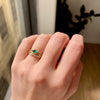 3 of 3: A vibrant emerald set in a bezel setting with engraved lines, flanked by two round diamonds and pave diamonds on either side, on hand