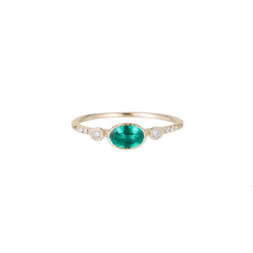 A vibrant emerald set in a bezel setting with engraved lines, flanked by two round diamonds and pave diamonds on either side.