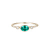 A vibrant emerald set in a bezel setting with engraved lines, flanked by two round diamonds and pave diamonds on either side.