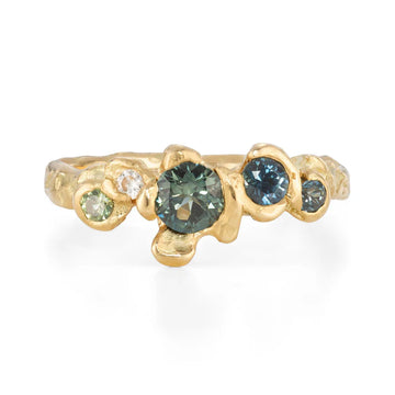 Organically shaped gold band set with four green and blue sapphires, and one white diamond. 