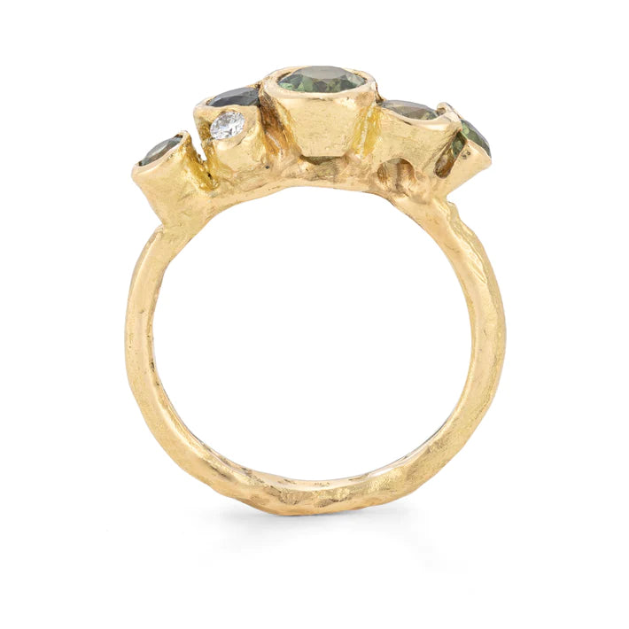 Gold organically carved band with five bezel set green sapphires and one white diamond.