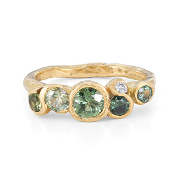 Gold organically carved band with five bezel set green sapphires and one white diamond.