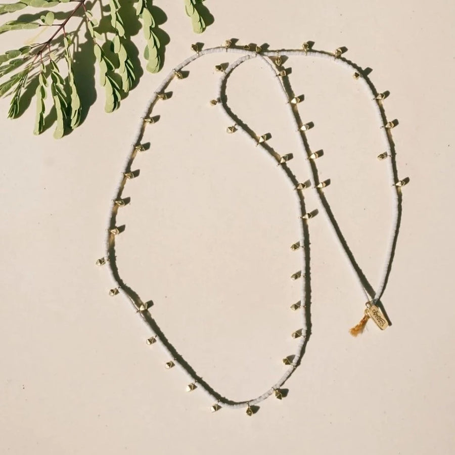White matte glass beads interspersed with brass beads that hang down, on silk cord