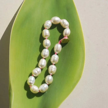 Pearls strung on hot pink cord with knots tied between each one, and a brass button clasp