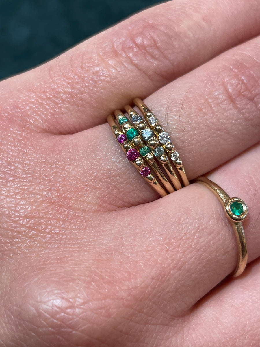 Close-up of a hand wearing multiple gold rings with gemstones on a neutral background