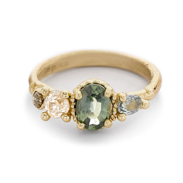 A pretty four stone engagement ring with sapphires in soft tones of green and neutral toned diamonds with decorative settings in yellow gold, on a matte gold band. 