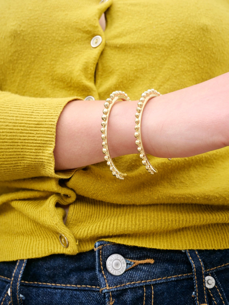 two knobbly brass cuffs on model with yellow sweater