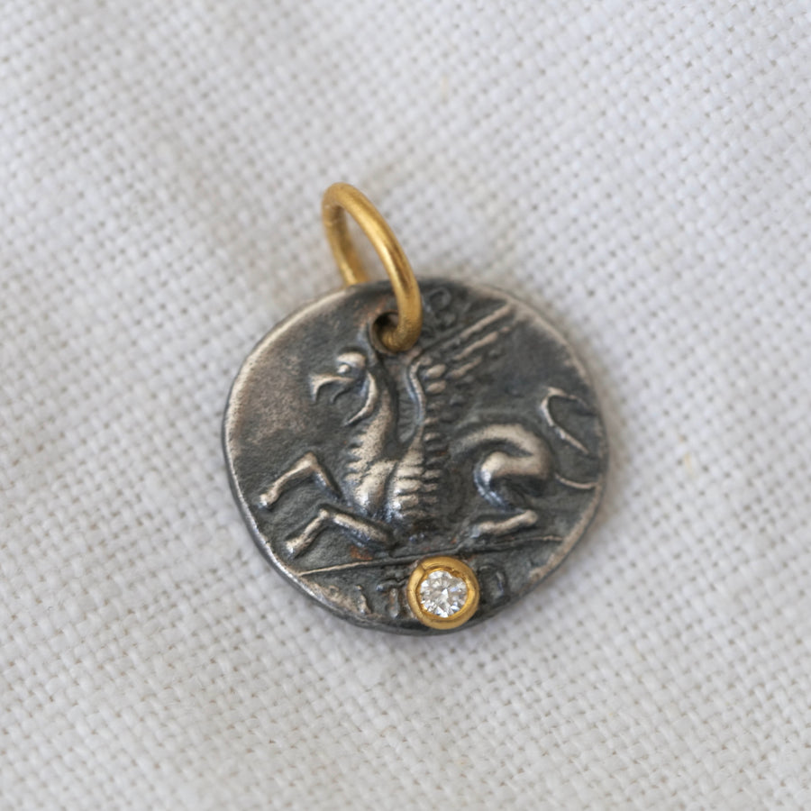 oxidized sterling silver coin with a pegasus and bust design, accented by a sparkling diamond in 24K gold