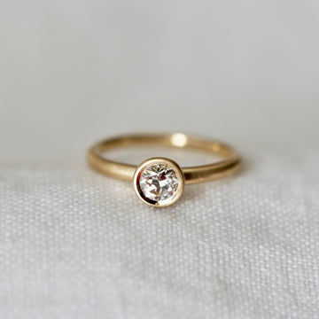 Bezel set solitaire diamond ring on white linen background