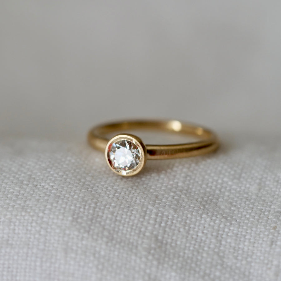 Bezel set solitaire diamond ring on white linen background