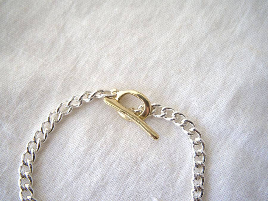 Silver chain bracelet with a gold clasp on a light gray fabric background