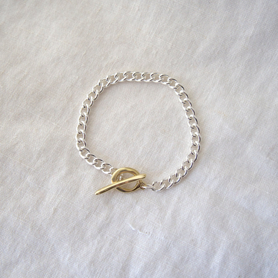 Silver chain bracelet with a gold clasp on a light gray background